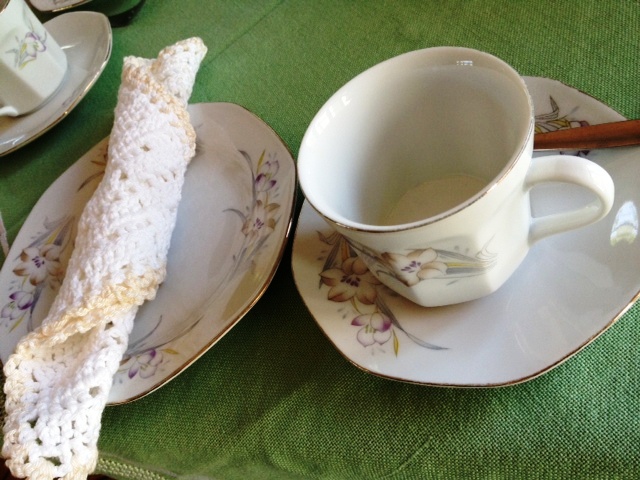 Gammeldags kaffekop og hjemmehæklet serviet på grøn dug 